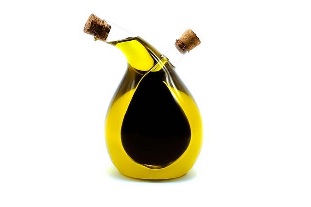 Elegant dark glass bottle of extra virgin olive oil from Andalusia Spain with handwritten label surrounded by fresh green olives and olive branches on rustic wooden surface