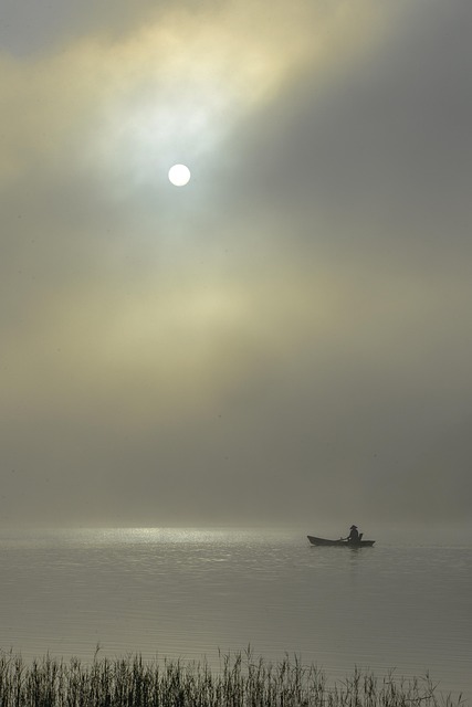 Small fishing boat at dawn on the coast of Brittany France with a fisherman harvesting fleur de sel from shallow salt pans as the sun rises over calm water