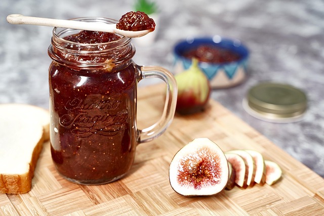 Glass jar of homemade wild fig preserve with visible whole fig pieces and a warm amber colour, beside fresh ripe figs cut in half on a linen napkin with cheese board