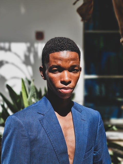 Professional headshot portrait of a South Asian man in his mid-forties wearing a navy blue linen shirt, standing in a modern bright office space with shelves of specialty food products in the background, warm natural smile