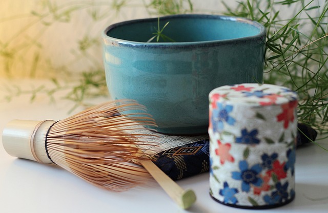 Ceremonial grade Japanese matcha powder in a traditional ceramic chawan bowl with bamboo whisk chasen beside it on a minimalist light wood surface with soft natural lighting