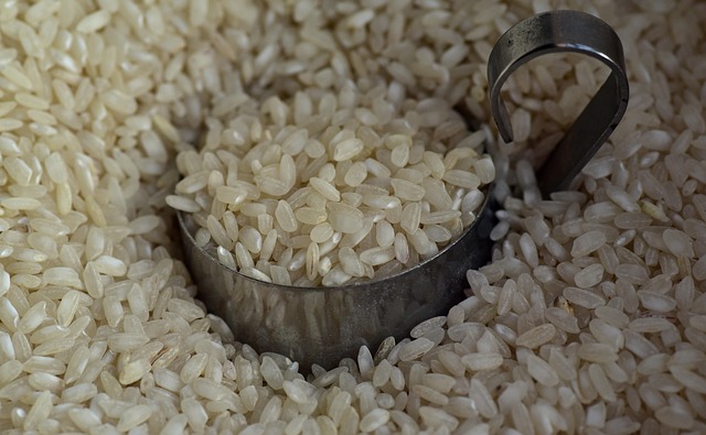 White cotton bag of Italian farro perlato pearled ancient grain with some grains scattered on a wooden cutting board beside a rustic ceramic bowl and wheat stalks
